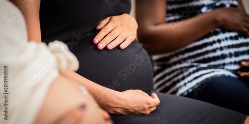 Quadro su tela Close-up of three pregnant women sitting, hands on their bellies.