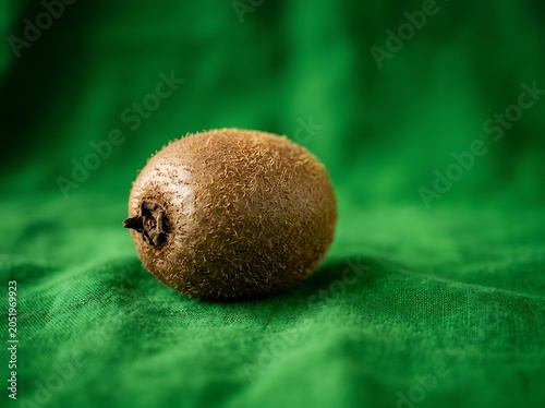 Whole kiwi fruit on green textured fabric background