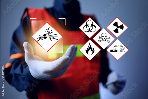Worker wearing a high visibility vest and protective glove holding a virtual interface displaying GHS hazard symbols for explosives, biohazards, radiation, fire, toxic materials, and corrosives