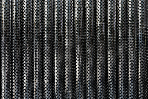 Industrial Perforated Metal Pipes Pattern Background. Close-up texture of industrial stainless steel pipes with a repeating pattern of circular perforations, suitable for abstract design backgrounds.