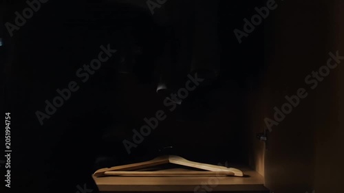 Empty wooden hanger lying in a dark wardrobe with hanging clothes.
