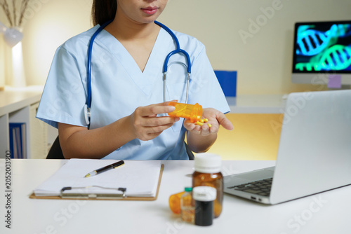 Foto A healthcare professional in blue scrubs and stethoscope pours capsules from an orange pill bottle at a clinic desk, ideal for pharmacy and medical content