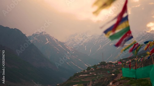 4K Landscape shot of orange clouds surrounding the snowy Himalayan mountain peak during a stormy weather with defocused Buddhist prayer flags waving in the front as seen from Lahaul in Himachal, India