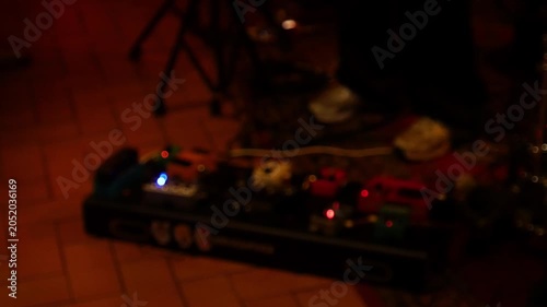 Blurred defocused guitar effect pedal board with glowing indicator lights on floor during live music band performance night