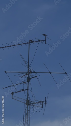 Old rooftop television antenna with multiple elements against clear blue sky and white clouds urban residential communication