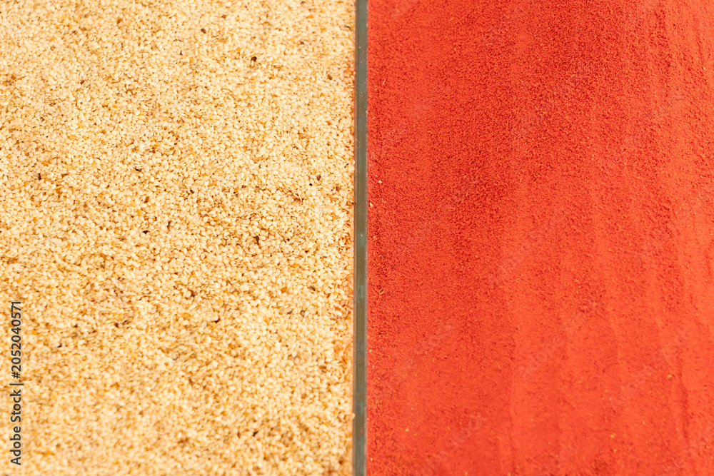 Fototapeta premium Contrast background pattern of organic white sesame seeds and vibrant red paprika powder. Top view texture of oriental spices for food design layout