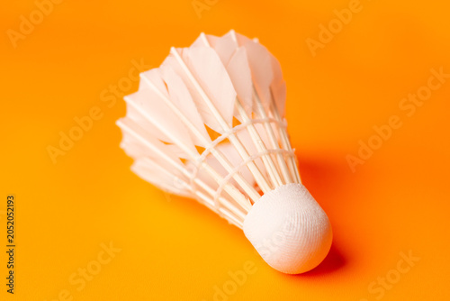 High angle view of a white badminton shuttlecock with its cork pointing diagonally downward toward the bottom left on an orange surface.