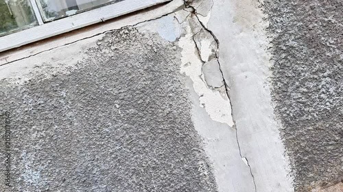 Exterior wall of an aging building showing cracked plaster, rough textured stucco, and visible structural wear beneath a window. Urban decay, maintenance issues, and weather damage