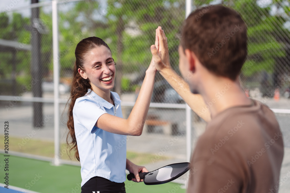 Obraz premium Pickleball doubles team celebrating victory on outdoor court. Smiling man and woman greeting during active fitness match.