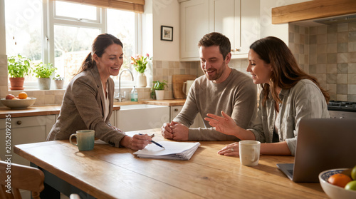 Couple meeting financial advisor at kitchen table reviewing paperwork laptop home loan planning insurance budget guidance family investment consultation property decision support future