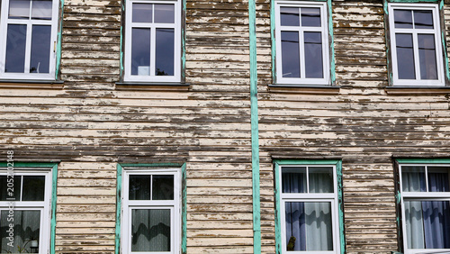 Old wooden building facade featuring distressed horizontal planks with chipped paint, framed by white windows and green trim, creating a textured background