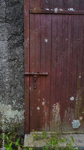 Close-up of a thick iron door covered with rust and secured by a locked padlock. The weathered metal surface, corrosion patterns, and strong industrial appearance convey themes of security, protection