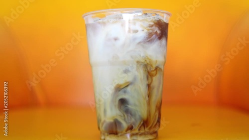 4K Pouring fresh milk into plastic cup of iced black coffee Refreshing iced latte drink isolated on vibrant yellow and orange background.