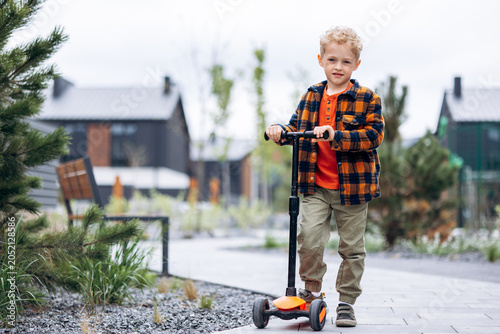 Φωτογραφία Smiling young boy wearing casual clothes standing with his three-wheeled scooter