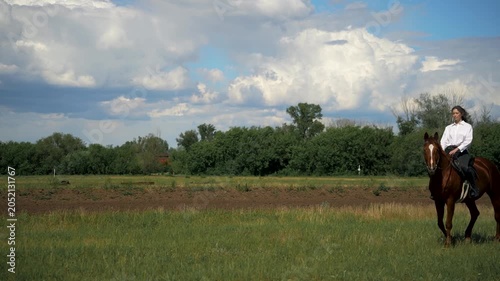 Woman riding a brown horse in a grassy field.