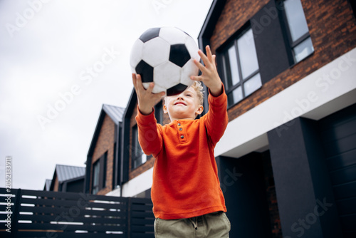 Obraz na plátne Boy catching soccer ball with both hands in a residential neighborhood, enjoying