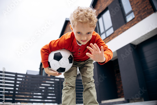 Photography Happy child with curly hair holding a soccer ball, enjoying active playtime and
