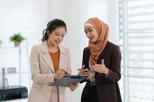 Fotografía Two business colleagues multiethnic working in office, asian muslim