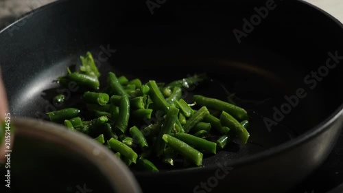 Green bean cooking. Hand puts green bean pods in a frying pan