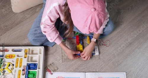Girl wearing pink cap and smart watch connecting electronic circuit blocks to assemble radio transmitter. Educational STEM activity for physics learning or engineering hobby promo. Real lifestyle