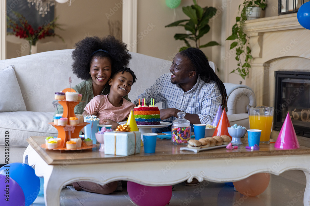 Obraz premium African American family leaning toward table in living room celebrating birthday with rainbow cake