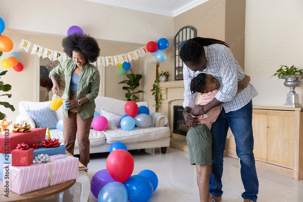 Obraz premium African American family celebrating birthday in living room with banner, woman pouring from pitcher