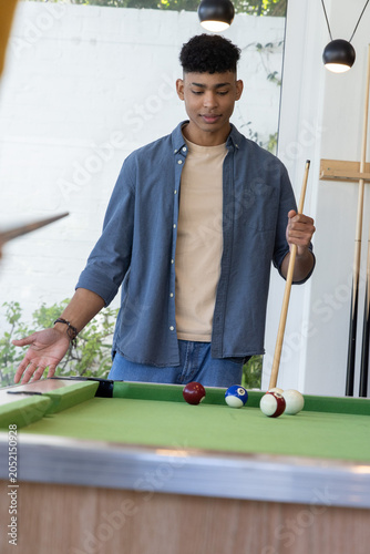 African American teen standing at green-felt pool table holding cue, eyeing balls under pendants