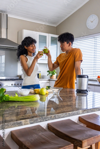 Diverse couple toasting blender juice on granite island after blending apple and celery for health