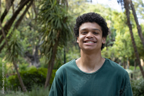 Adult African American man standing, smiling in park wearing green crewneck tee near lamp post