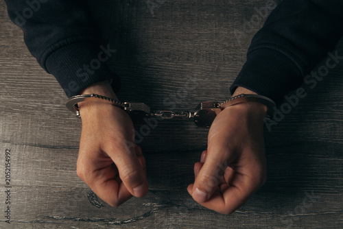 Фотография Hooded man in handcuffs on dark background. Criminal concept.