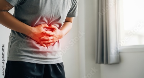 Closeup of a person suffering from severe abdominal pain, stomach ache, or indigestion, holding their stomach with both hands