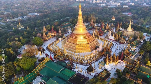 Aerial drone view at Shwedagon Pagoda, a golden stupa, surrounded by lush greenery and urban development in Yangon (Rangun), Myanmar (Burma), showcasing the city's blend of religious and modern life.