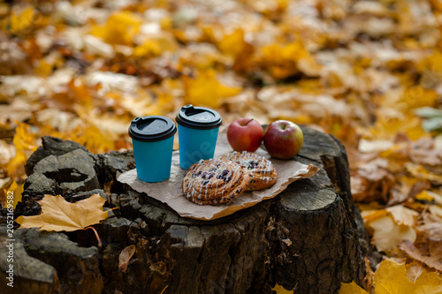 Autumn picnic concept - cups, pastries, and apples on old tree stump among colorful leaves