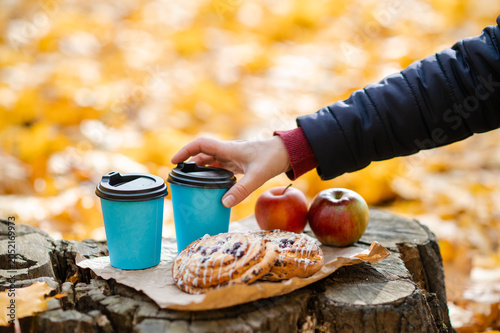 Autumn picnic concept - female hand reaching for cup on tree stump with pastries and apples among colorful leaves