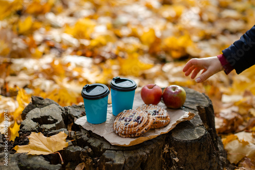 Autumn picnic concept - female hand reaching for cup on tree stump with pastries and apples among colorful leaves