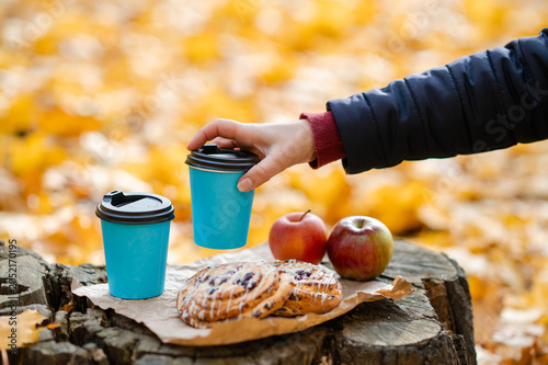 Autumn picnic concept - female hand reaching for cup on tree stump with pastries and apples among colorful leaves