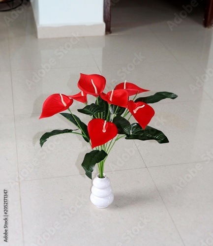 Schilderij op canvas wide petalled beautiful silk-made artificial red flowers with wide green leaves, planted in a decent white ceramic vase
