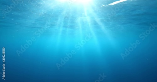 Sun rays shining through clear blue ocean water, underwater light background


