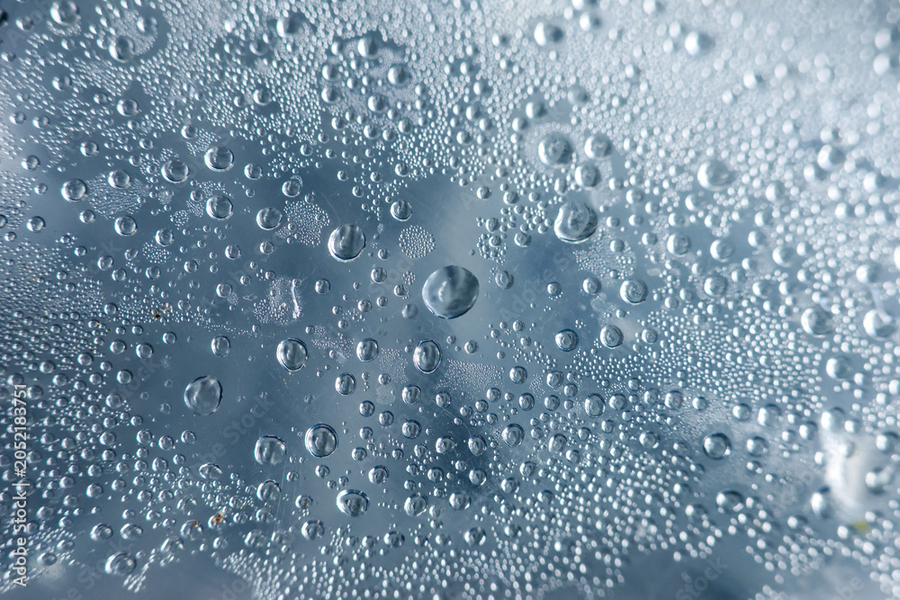 Fototapeta premium Close up view of wet water droplet and tiny bubble on blue glass surface showing condensation from heavy rain, evoking calm, serene and peaceful mood