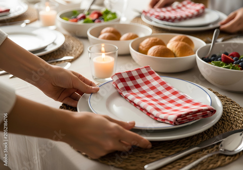 Woman sets table with plates, napkins, and food at candlelit dinner with rolls and salad.
