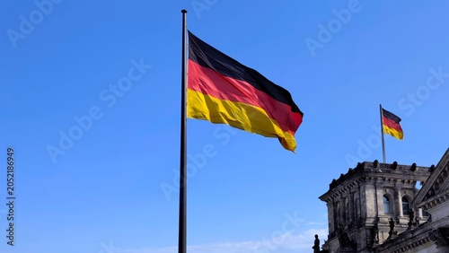 Fotografija Photo of the German national flag waving proudly against a clear blue sky outside the historic Reichstag building in Berlin, Germany