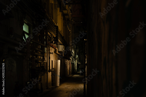 Foto A narrow service alley between building backs in Wan Chai, Hong Kong Island, at night, with dense exposed pipework, ducting, and utility infrastructure lining the left wall