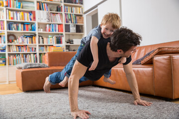 Father doing push ups in living room with son on his back