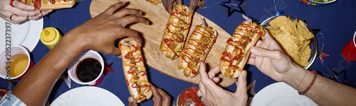 Website header shot of diverse young adults sharing hot dogs and snacks during Independence Day home celebration, symbolizing holiday gathering. Ideal for holiday marketing and social campaigns
