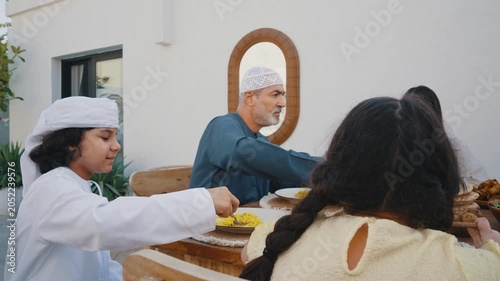 Arab family wearing traditional emirati clothing having lunch at home in the backyard garden - Middle-eastern family bonding and having fun on a family reunion dinner