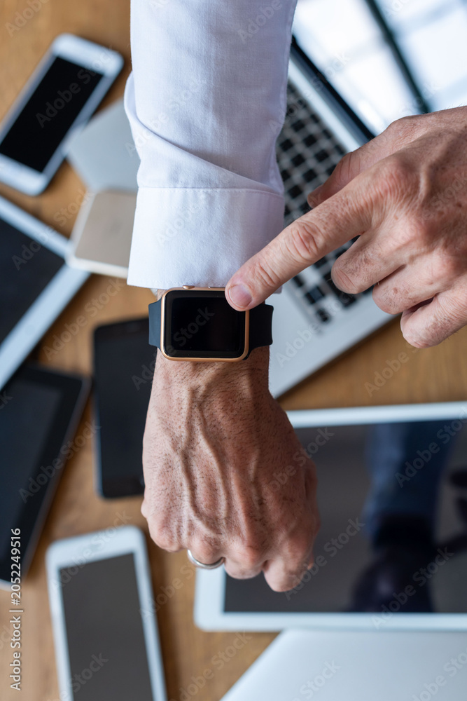 Naklejka premium Close-up of a person pointing at a smartwatch among various devices.