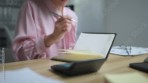 Close up of a female accountant using a calculator for budget management and taking notes in her agenda while working late at the office desk