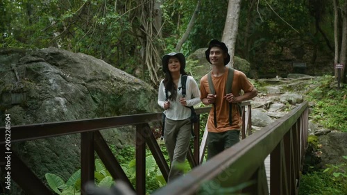 Enthusiastic young couple with backpacks walking together on a wooden walkway, exploring a tropical rainforest on an adventurous holiday