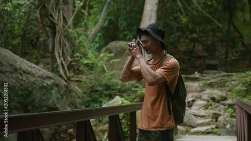 Young male traveler photographing nature while walking on a wooden bridge in a peaceful tropical forest