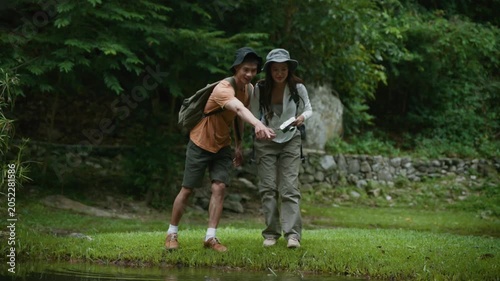 Excited couple enjoys skipping stones together on a peaceful pond while exploring a vibrant, verdant forest during a hike